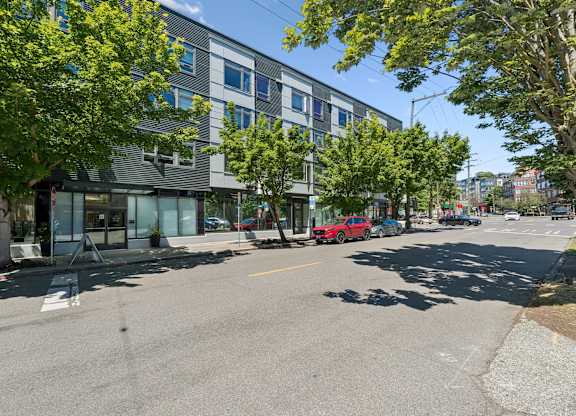 A street view with a building on the left and a red car on the right.
