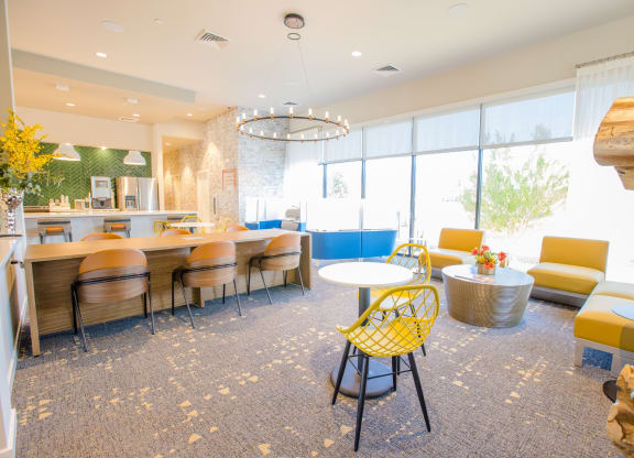 a lounge area with yellow chairs and tables and a kitchen with large windows
