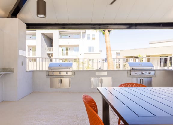 a patio with a table and chairs and two barbecue grills