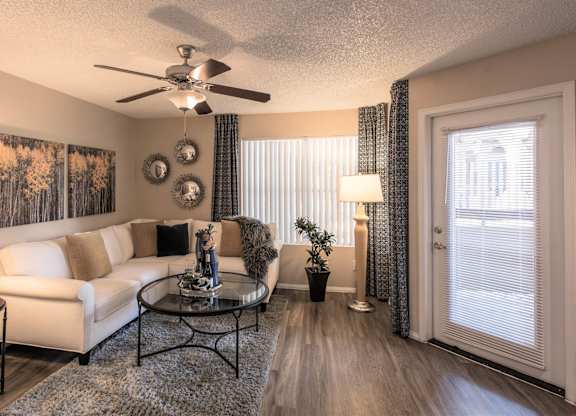 Apartments in Ahwatukee, Foothills, AZ - Pacific Bay Club - Living Room with Wood-Style Plank Flooring, Stylish Decor, Ceiling Fan, Large Window, and Door to the Private Patio