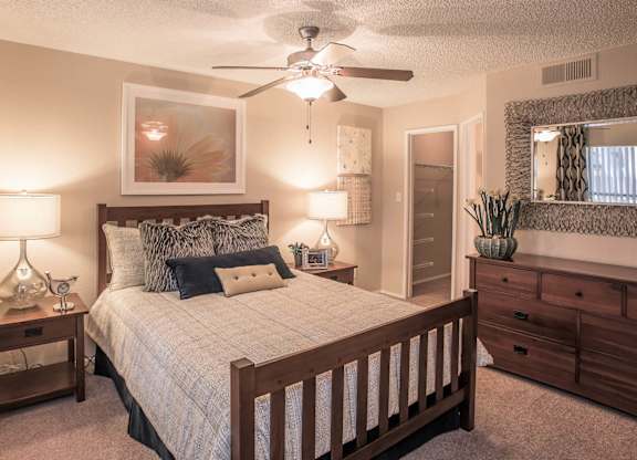 Apartments Ahwatukee, AZ - Pacific Bay Club - Bedroom with Carpeted Flooring, Bed, Wooden Nightstands with Lamps, Dresser, Framed Mirror, Ceiling Fan, and Large Closet.