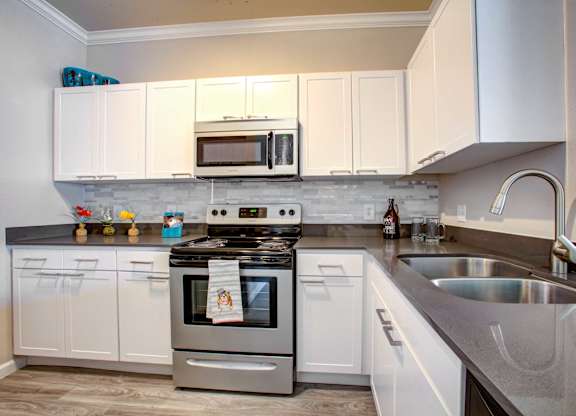 North Phoenix AZ Apartments for Rent - Ironhorse at Tramonto - Kitchen with Wood-Style Flooring, White Cabinetry, Grey Quartz Countertops, Stainless Steel Appliances, Light Tile Backsplash, and Silver Hardware