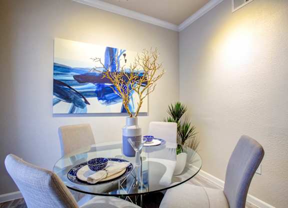North Phoenix, AZ, Apartments for Rent - Ironhorse at Tramonto - Dining Area with Round Glass Table, Grey Chairs, Houseplant, and Wall Art.