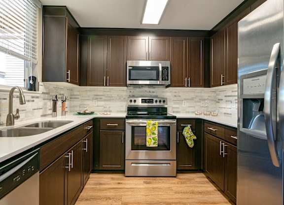 Walnut Creek, CA, Apartments - Ivy Hill - Kitchen with Hardwood Floor, Stainless Steel Appliances, Tile Backsplash and White Countertops, and Large Window above Double Sink.