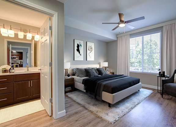 Apartments in Walnut Creek, CA - Ivy Hill - Spacious Bedroom with Hardwood Floor, Area Rug, Ceiling Fan, Bed, Nightstands with Lamps,  Large Windows, and Attached Bathroom.
