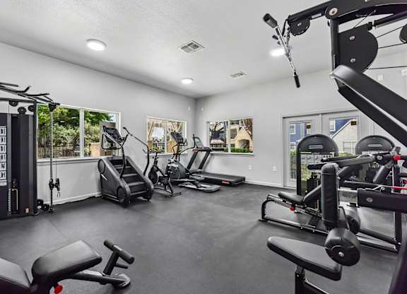 A spacious gym with various exercise equipment and a view of trees outside the windows.