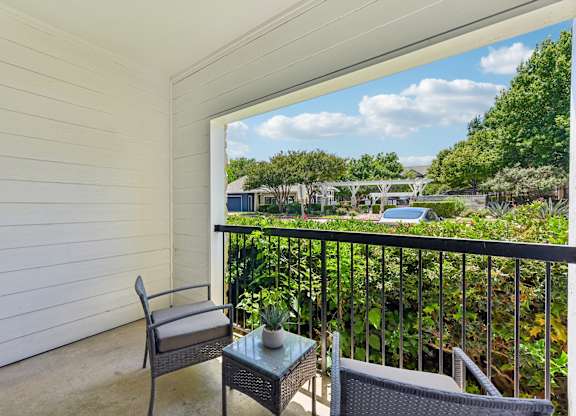 A balcony with a chair and table overlooking a green landscape.