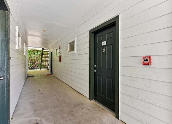 A hallway with a black door and a fire extinguisher on the wall.