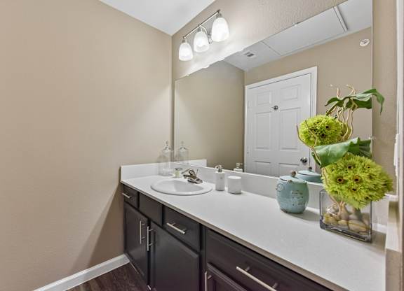 A bathroom with a sink, mirror, and a vase of flowers.