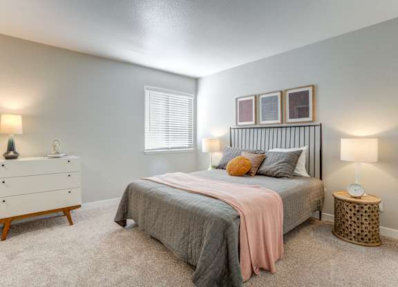 Mountain Park, OR, Apartments - MiLO - Mountain Park, OR Apartments - Spacious Bedroom With Plush Carpet Flooring, Bed, Nightstands with Lamps, Dresser, And Window.