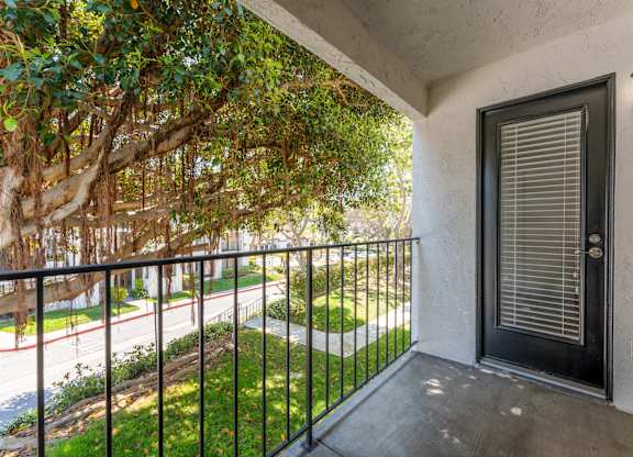 a balcony with a black railing and a door and a tree