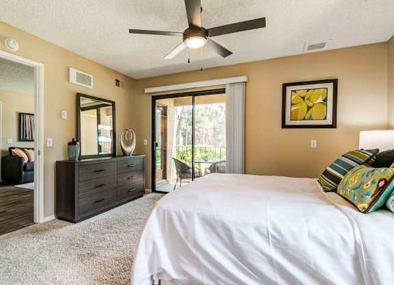 Pet-Friendly Apartments in La Jolla, CA - Mirada at La Jolla Colony - Bedroom with Direct Patio Access, a Ceiling Fan, and Plush Carpet Flooring