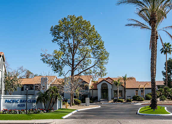 Ahwatukee, AZ, Apartments for Rent - Pacific Bay Club - Property Exterior with White Walls, Terracotta Roofing, Driveway, and Palm Trees.