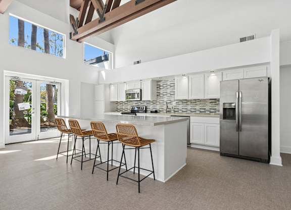 A kitchen with white cabinets and a large island with a refrigerator on the side.