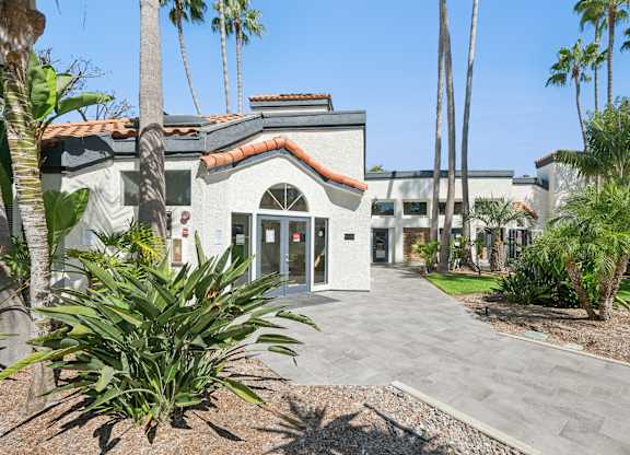 A building with a red tile roof and palm trees in front.