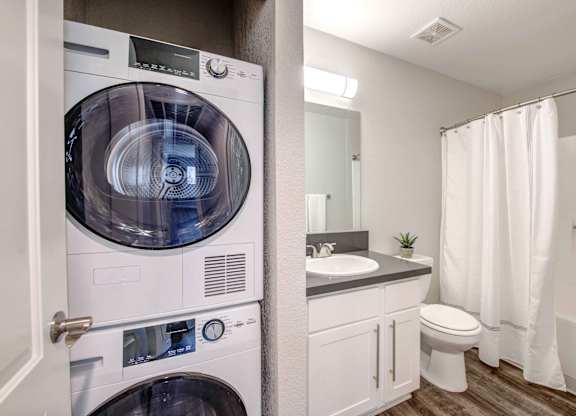 Apartments in San Clemente, CA - Rancho Del Mar - Bathroom with Hardwood-Inspired Flooring, a Toilet, a Shower, a Vanity with White Cabinets, and an In-Unit Washer/Dryer