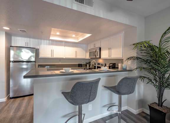 One-Bedroom Apartments in San Clemente, CA - Rancho Del Mar - Modern Kitchen with White Cabinets, Stainless Steel Appliances, Grey Countertops, High Top Seating, and Stylish Decor