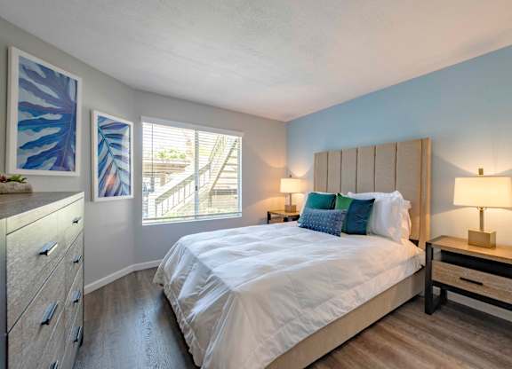 Apartments in San Clemente for Rent - Rancho Del Mar - Spacious Bedroom with Large Window, Wood-Style Flooring, and Light Blue Accent Wall