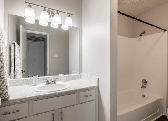 A white bathroom with a sink, mirror, and bathtub.