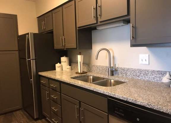A kitchen with a black refrigerator and brown cabinets.