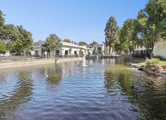 A serene pond with a fountain in the middle surrounded by trees and buildings.