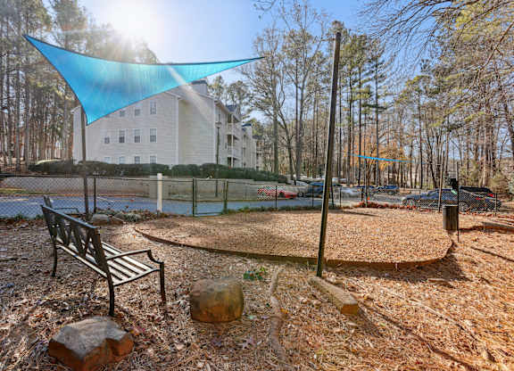 A park with a bench and a blue shade sail.