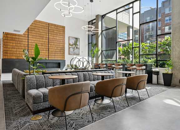 A modern living room with a grey sofa, brown chairs and a glass wall.