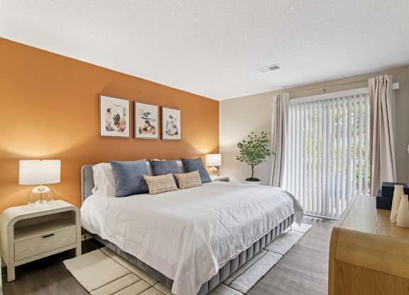 A bedroom with a large bed, a nightstand, and a window with curtains.