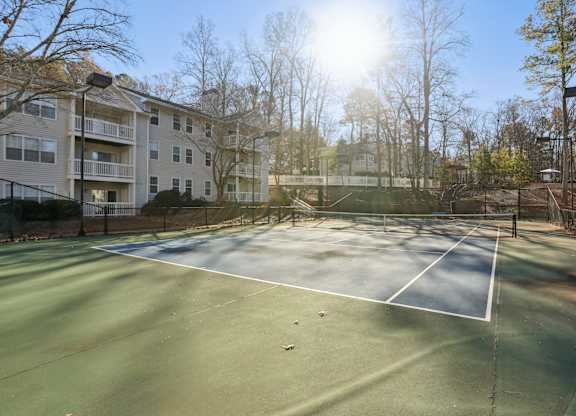 A tennis court is surrounded by apartment buildings.