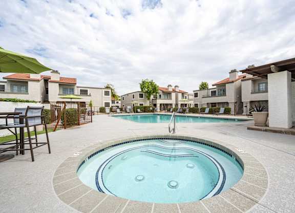 Apartments Scottsdale, AZ - The Sycamore at Scottsdale - An exterior view the pool with gated entry featuring lounge seating, umbrellas, and nice landscaping