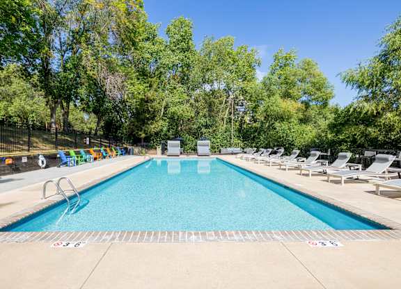 A large swimming pool surrounded by trees and lounge chairs.