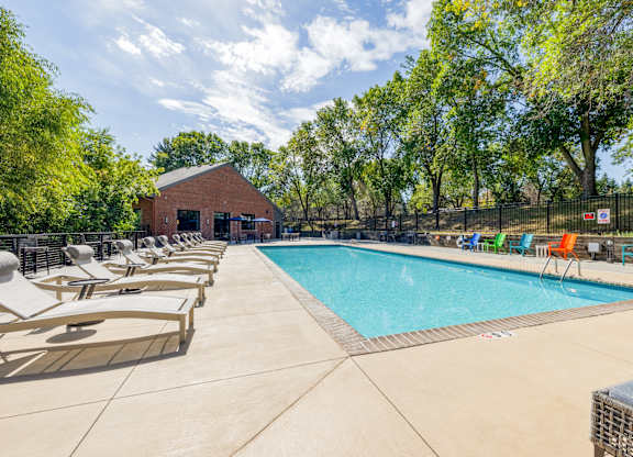 A pool surrounded by chairs and trees with a building in the background.