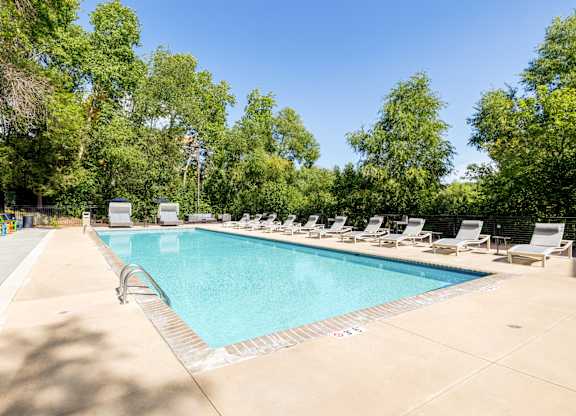 A large swimming pool surrounded by trees and lounge chairs.