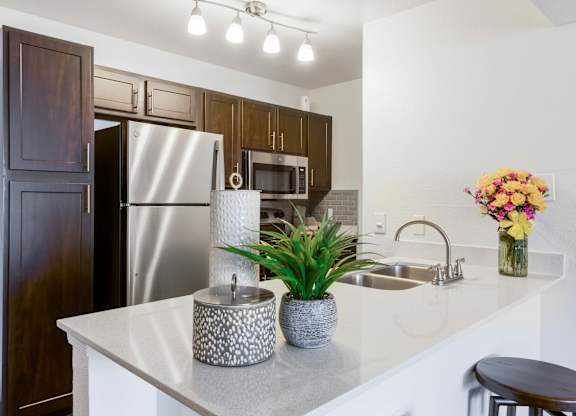 Apartments for Rent Scottsdale, AZ - The Sycamore at Scottsdale - Kitchen with Stainless Steel Appliances, Dark Wood-Tone Cabinetry, White Quartz Countertop,  Kitchen Island with Dual Sink, and Overhead Lighting Fixture.