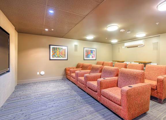 a spacious theater room with orange couches and a tv