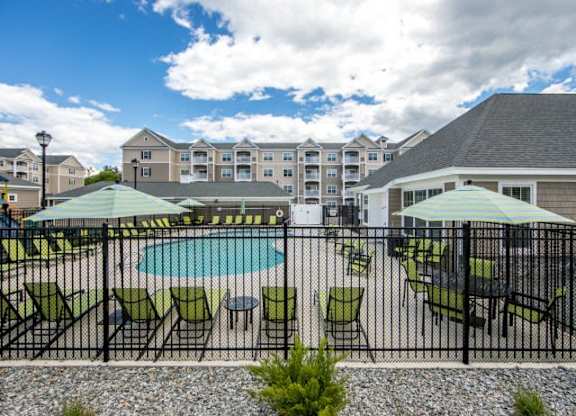 a pool with green chairs and umbrellas in front of a building