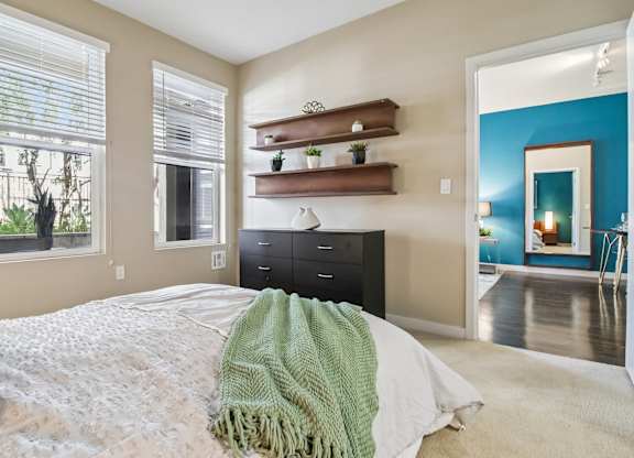 A bedroom with a bed covered in a white blanket and a green throw.