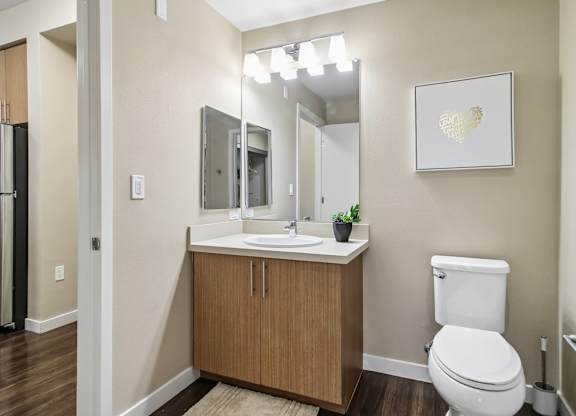 A bathroom with a white toilet, a wooden cabinet, and a framed picture on the wall.
