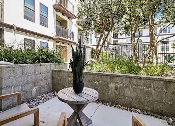 A patio with a table and chairs surrounded by a wall and plants.