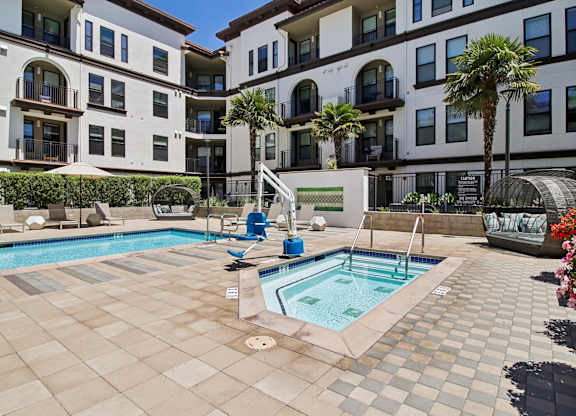 A pool surrounded by a tiled patio and a building with balconies.