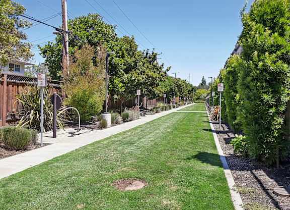 A long, narrow, green lawn runs down the center of a tree-lined street.