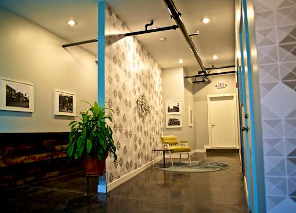 A hallway with a plant, pictures, and a yellow chair.