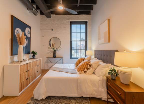 A bedroom with a large bed, a wooden dresser, and a painting on the wall.