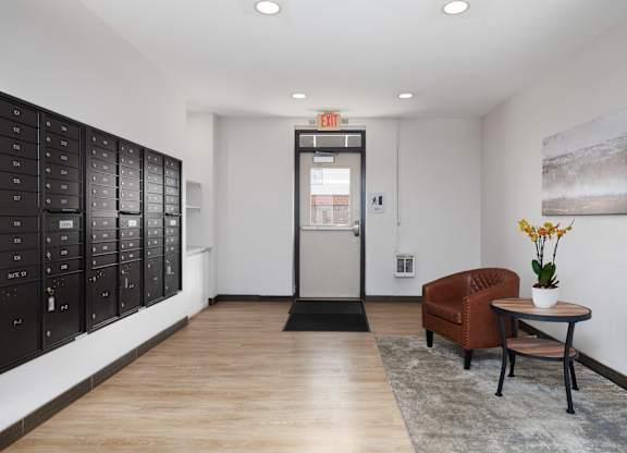 A hallway with a brown chair, a table with a vase of flowers, and a wall with a painting.