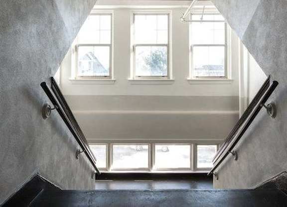 A staircase with a black railing leads to a bright room with three windows.