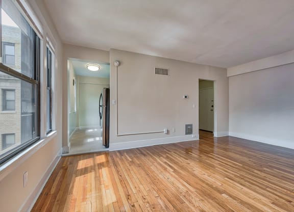 an empty living room with wood flooring and a large window at The Argonne Apartments, Washington DC