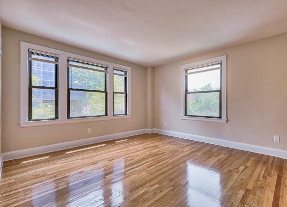 an empty living room with wood floors and three windows at The Argonne Apartments, Washington DC