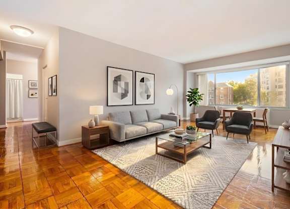 A living room with a grey sofa, a grey couch, a grey chair, a grey rug, a grey coffee table, a grey floor lamp, a grey wall, a grey door, a grey wall, a grey wall, a grey