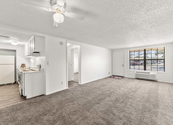 an empty living room with a kitchen and a ceiling fan