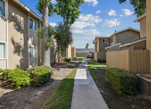 a pathway between two apartment buildings with trees and grass